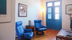 Una habitación con dos sillones azules, una mesita con lámpara y suelo de madera.