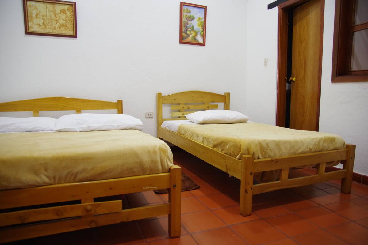 Two wooden beds with white bedding, a wooden door, and two framed pictures on the wall.