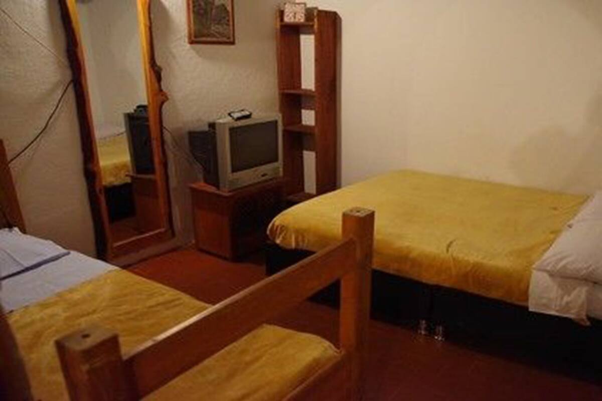 A small, simple room with two single beds, a wooden chair, a television, and a mirror.