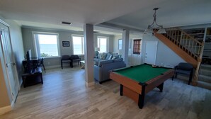 A spacious living area with a pool table, a sofa set, and a staircase leading to a loft. - Oceanfront House with Private Beach, Patio, and Gameroom (Ponte Vedra Beach)