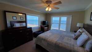 A bedroom with a bed, dresser, TV, and a ceiling fan. It has large windows with a view of the beach. - Oceanfront House with Private Beach, Patio, and Gameroom (Ponte Vedra Beach)
