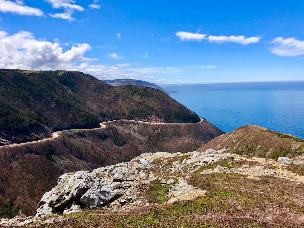 Paisagem montanhosa com estrada sinuosa e vista para o mar.
