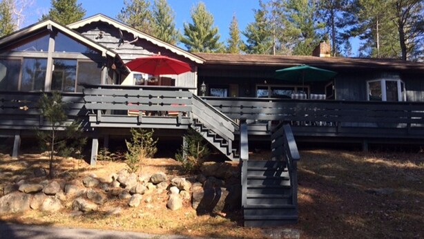 Un chalet avec une façade en bois, un escalier menant à une terrasse et un parasol rouge sur la terrasse.