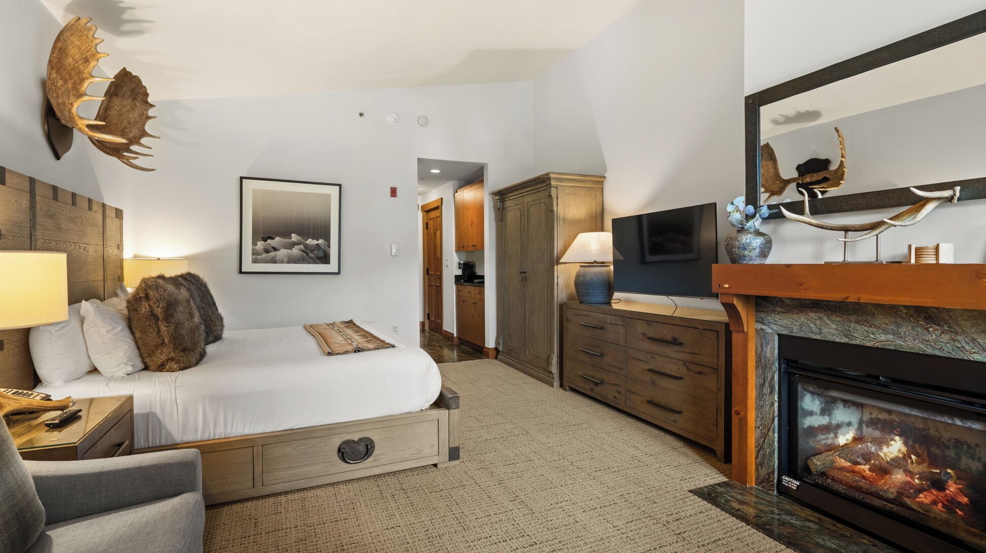 A modern hotel room with a bed, a fireplace, a TV, and a large mirror.