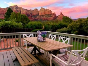 A wooden deck with a table and chairs, overlooking a mountainous landscape.