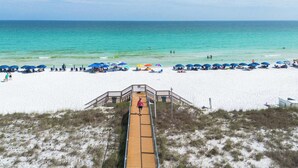 A beach with a wooden boardwalk leading to the water, surrounded by beach umbrellas and chairs.