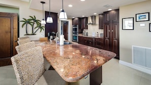 A kitchen with a granite island, dark wooden cabinets, and pendant lighting.