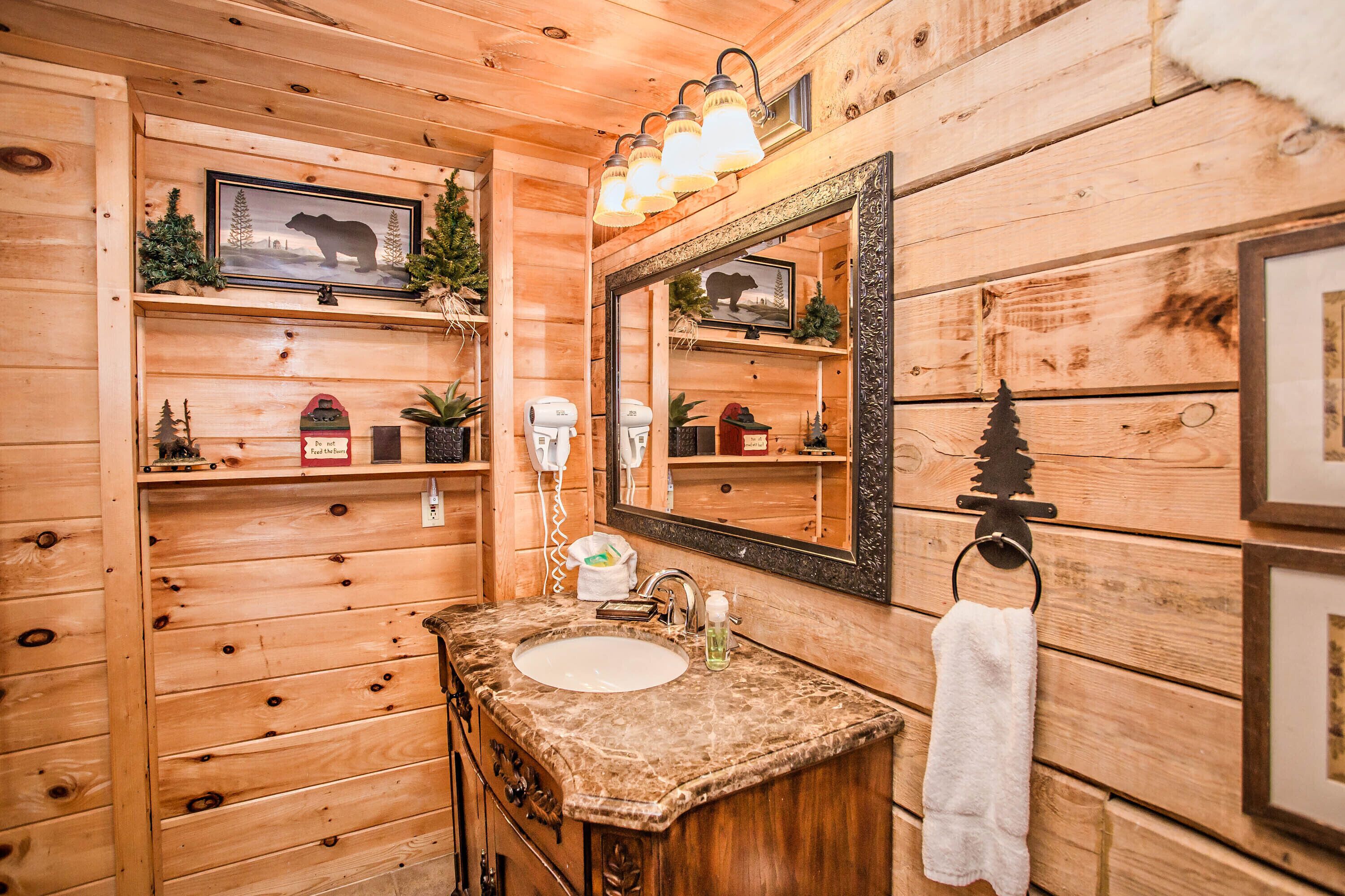 Une salle de bain rustique, aménagée dans une cabane en bois, avec un lavabo, un miroir et des étagères contenant des articles de toilette.