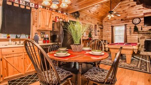 Ein Holzblockhaus-Innenraum mit Esstisch, Stühlen, einem Kühlschrank und einem Billardtisch.