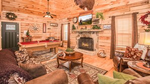 Ein gemütliches Blockhaus-Interieur mit Kamin, Holzwänden, einem Billardtisch und komfortablen Sitzbereichen.