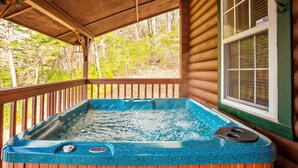 Ein Whirlpool auf einer Holzterrasse mit Blick auf einen Wald.