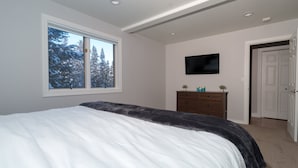 A bedroom with a bed, a dresser, a television, and a window with a view of trees. - Beautiful Home in McCall w/ family & living room and large backyard w/ firepit (Mccall)