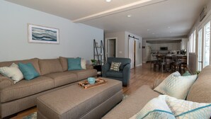A living room with a sofa, ottoman, and armchair, a dining area with a table and chairs, and a kitchen in the background. - Beautiful Home in McCall w/ family & living room and large backyard w/ firepit (Mccall)