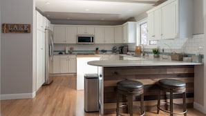 A modern kitchen with white cabinets, a stainless steel refrigerator, a microwave, and a wooden island with bar stools. - Beautiful Home in McCall w/ family & living room and large backyard w/ firepit (Mccall)