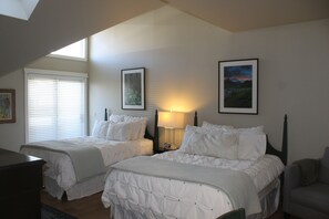 Guest room with two single beds, bedside table, and large window with blinds.