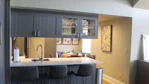 Une cuisine moderne avec des meubles gris, un plan de travail blanc et des tabourets de bar noirs.