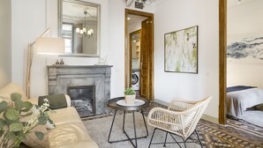 A room with a fireplace, a round table with a potted plant, a wicker chair, and a bed with a white blanket. - The Classic Apartment (Barcelona)