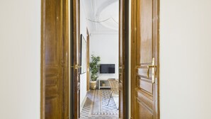 A hallway with wooden doors leading to a room with a television, a plant, and a chair. - The Classic Apartment (Barcelona)