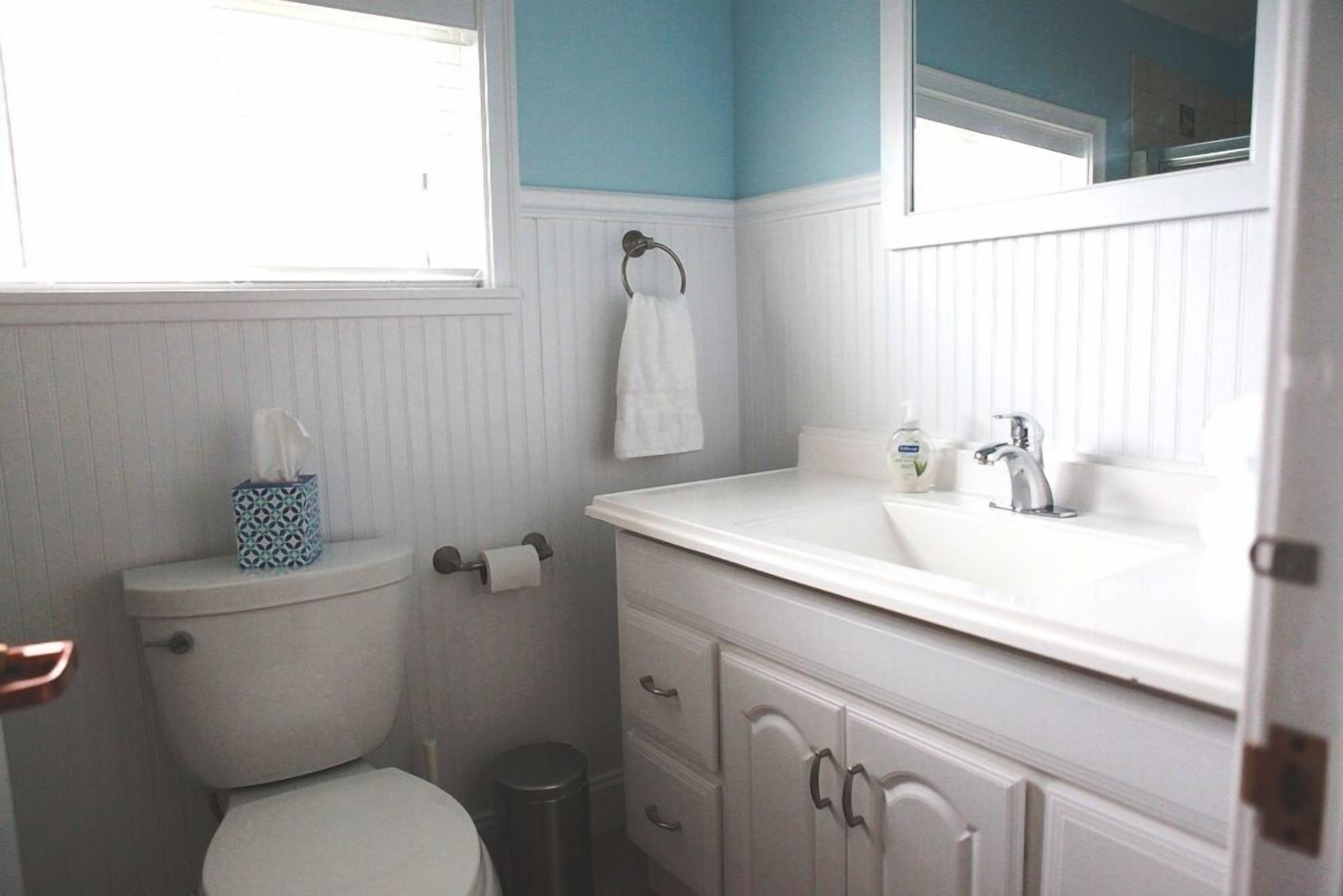 A bathroom with a toilet, a sink, a mirror, and a window.