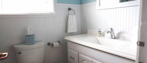 A bathroom with a toilet, a sink, a mirror, and a window.