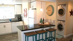 Una cocina con una isla central, taburetes de bar, lavadora y un reloj en la pared.