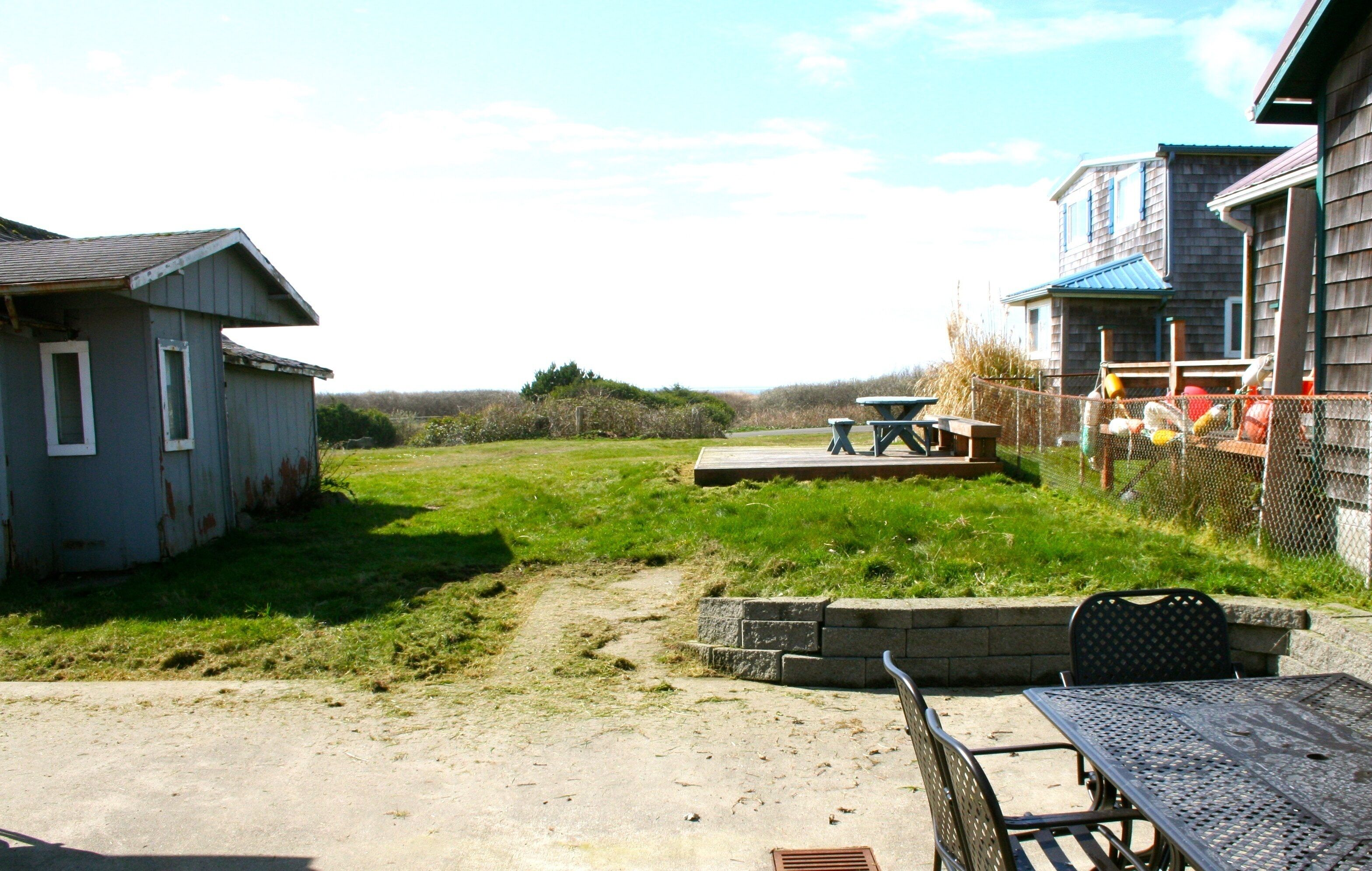 A rustic outdoor area with a concrete path leading to a wooden deck, surrounded by a chain-link fence.