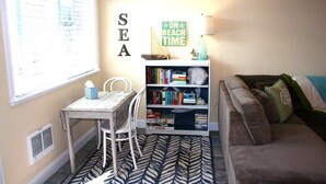 Una habitación con ventana, estantería, mesa y sofá.