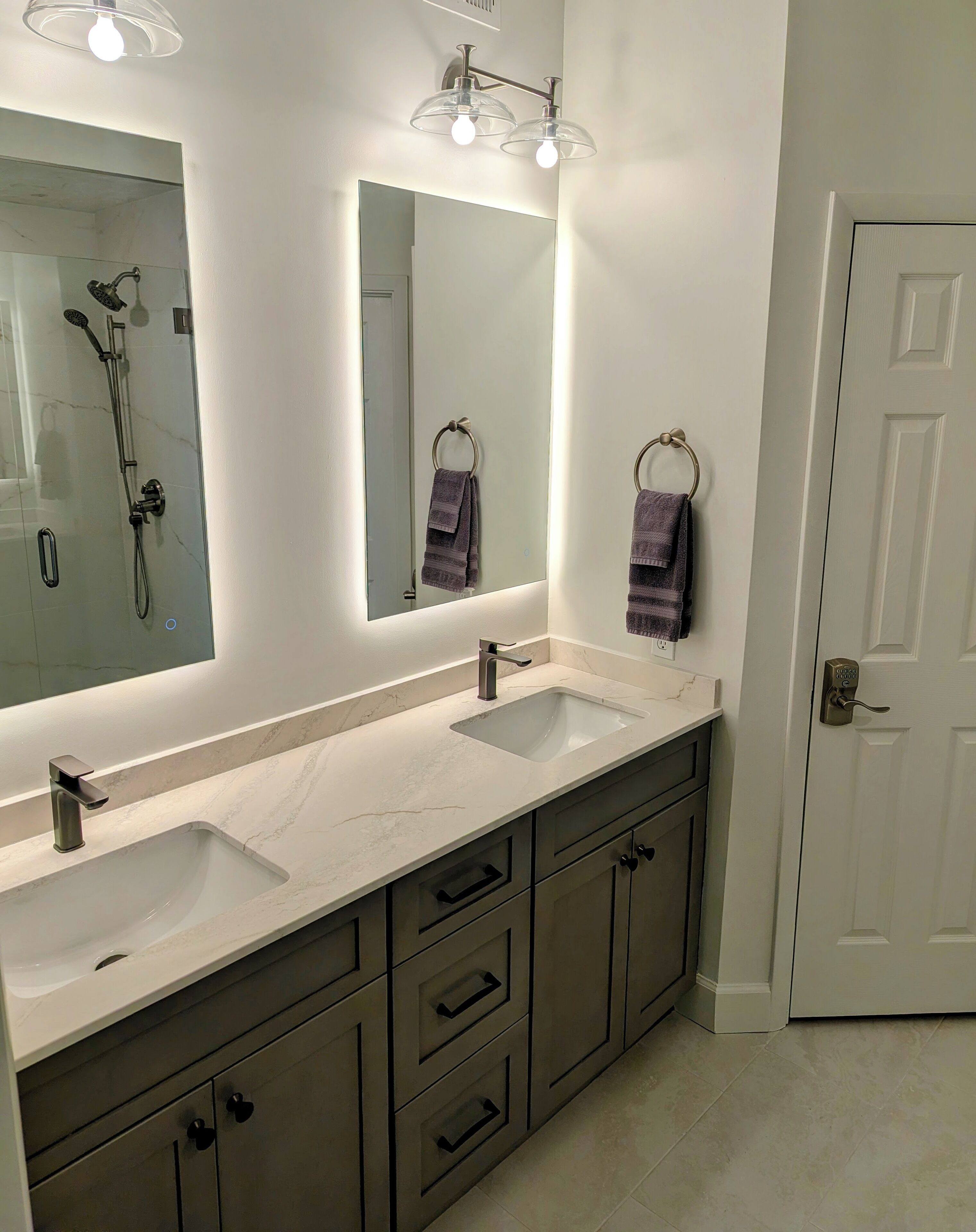 A bathroom with two sinks, a large mirror, a towel ring, and a shower.