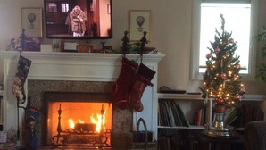 A cozy living room with a fireplace, a television mounted above it, and a decorated Christmas tree.