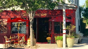 A café with outdoor seating, red awnings, and large potted plants.