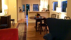 A spacious living room with a large rug, a dining area with a table set for two, and a kitchen in the background.