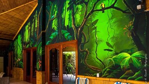 Una stanza con un grande affresco raffigurante una scena di bosco, porte in legno e un'area salotto con poltrone.