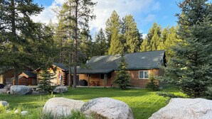Eine Blockhütte mit Veranda, umgeben von einem grasbewachsenen Hof und großen Steinen.