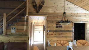 Ein Interieur einer Holzhütte, mit einer Holzvertäfelung, einer Treppe, einem Essbereich mit Ledersesseln und einer hängenden Leuchte.
