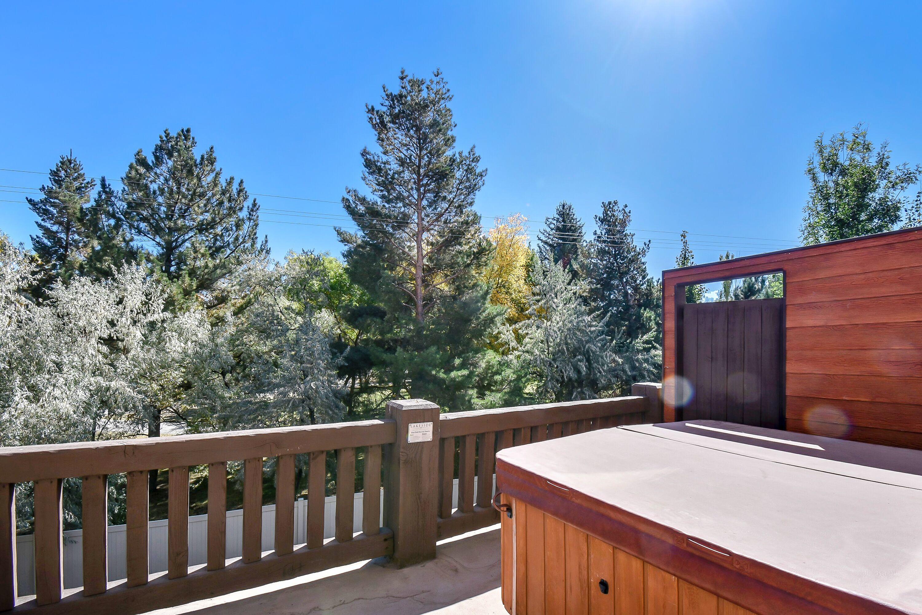 Eine Holzterrasse mit Whirlpool, umgeben von Bäumen und blauem Himmel.