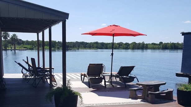 A wooden dock leading to a calm lake with a covered seating area featuring a red umbrella, lounge chairs, and a small table. - LBJ Waterfront Retreat-Large Quiet Cove, Great Views, Family Friendly, Discounts (Granite Shoals)