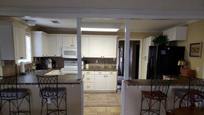 A kitchen with white cabinets, a black refrigerator, and a dining area with metal chairs. - LBJ Waterfront Retreat-Large Quiet Cove, Great Views, Family Friendly, Discounts (Granite Shoals)