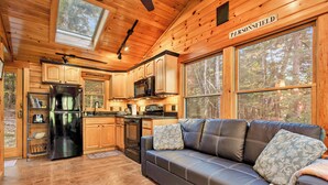 A log cabin interior with a kitchen, a leather sofa, and large windows. - Cozy riverfront cabin on Ossipee River (Parsonsfield)