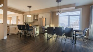A modern kitchen with dark wood flooring, white cabinets, and a central island with chairs. - Panoramic Mountain View 5BD 4.5BA Townhouse, Hot Tub, Near DT Canmore, Parking (Canmore)
