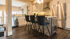 A modern kitchen with stainless steel appliances, a central island with bar stools, and a view to the living area. - Panoramic Mountain View 5BD 4.5BA Townhouse, Hot Tub, Near DT Canmore, Parking (Canmore)