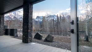A modern building with stone pillars, a covered patio, and a view of snow-capped mountains. - Panoramic Mountain View 5BD 4.5BA Townhouse, Hot Tub, Near DT Canmore, Parking (Canmore)