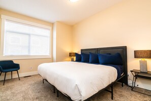 Un dormitorio con una cama, una silla, una mesita de noche y una lámpara.