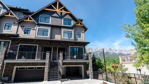 A multi-story house with a stone facade, a garage, and a staircase leading to the entrance. - Panoramic Mountain View 5BD 4.5BA Townhouse, Hot Tub, Near DT Canmore, Parking (Canmore)