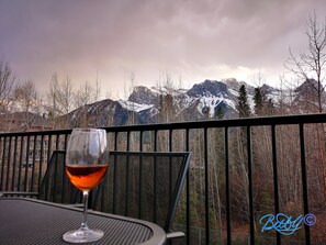 Una mesa con una copa de vino tinto y una silla, con vistas a un paisaje montañoso y una barandilla de metal.