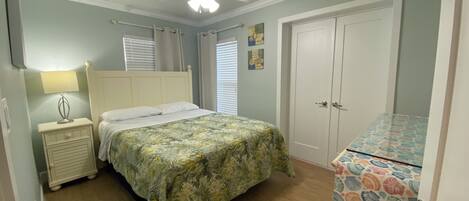 A bedroom with a bed, nightstand, lamp, ceiling fan, and a door with a patterned curtain.