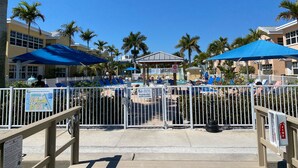 A pool area with umbrellas, palm trees, and a gated entrance. - 5 STAR RATED, GREAT PRICES NEW FULLY RENOVATED IS WAITING FOR YOU 3 BEDROOM E112 (Indian Shores)