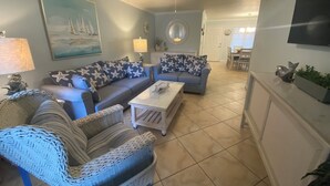 A living room with wicker furniture, a coffee table, a painting, and a ceiling fan. - 5 STAR RATED, GREAT PRICES NEW FULLY RENOVATED IS WAITING FOR YOU 3 BEDROOM E112 (Indian Shores)