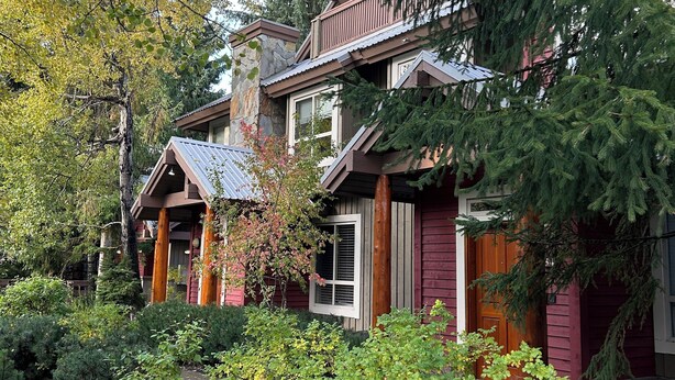 Een woonhuis met twee verdiepingen, een stenen schoorsteen, houten balkon en een tuin met diverse planten en een kleine vijver.