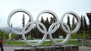 Een groot beeld van de Olympische ringen, buiten, met een verhard gebied en stenen trappen.