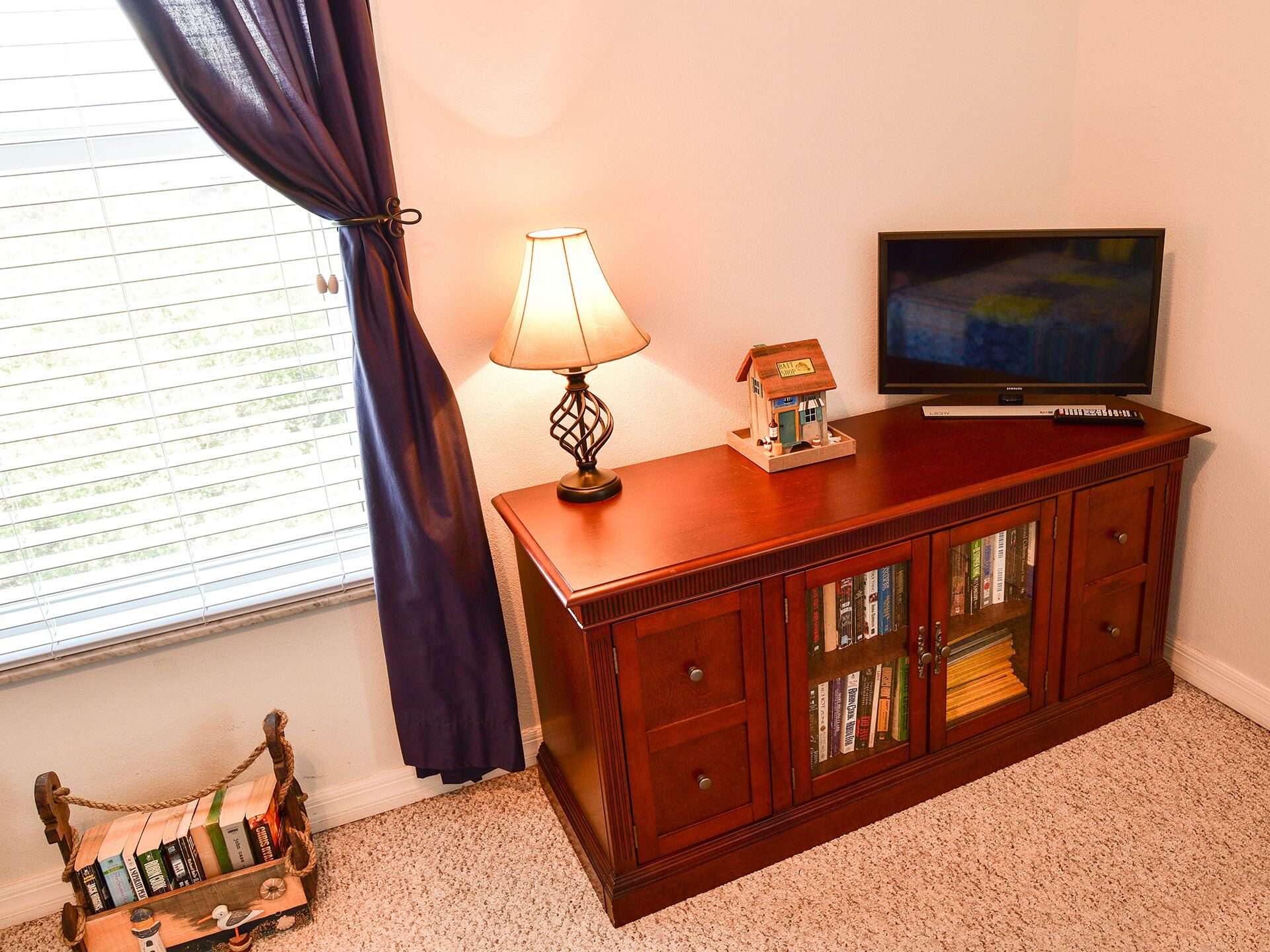 Un mueble de madera con un televisor encima, una lámpara y un pequeño modelo de casa.